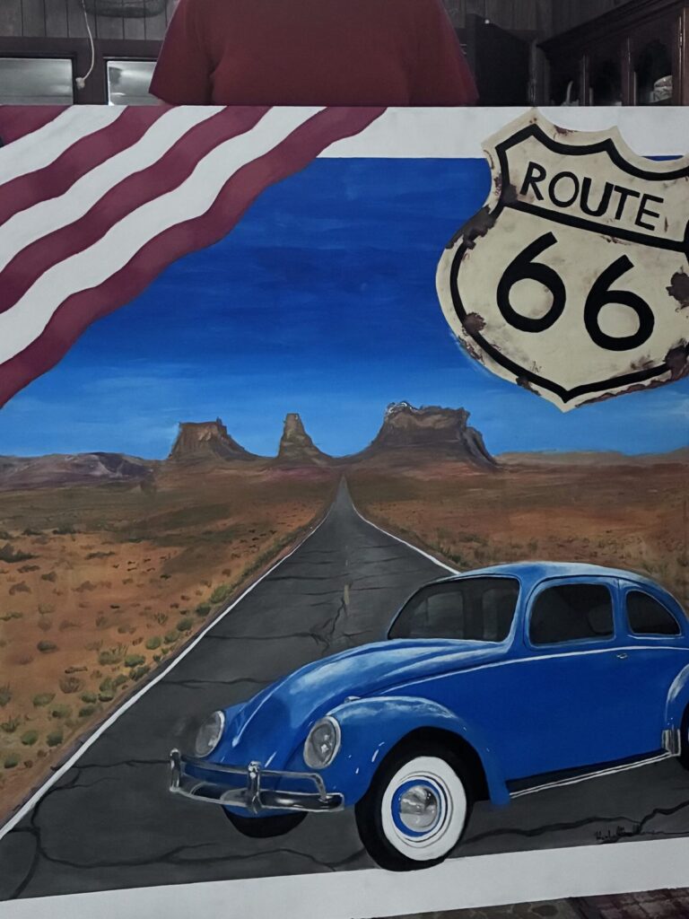 Painting of a blue VW Beetle on Route 66 with desert buttes and an American flag, created at the retreat's art class.