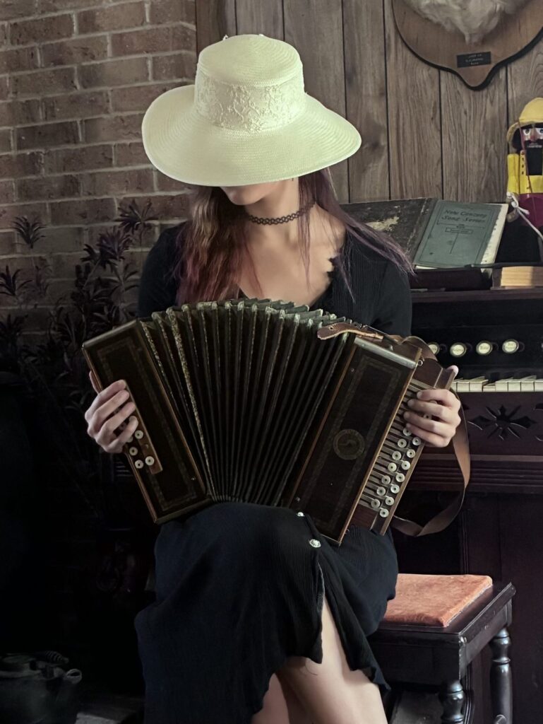 Music by the Fireplace Guest playing a vintage button accordion beside the antique pump organ and brick fireplace at the retreat.